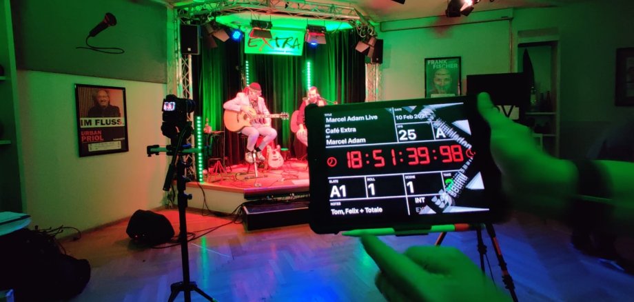 Bild von Aufnahme-Tag, Online Konzert Marcel Adam. Er ist im Hintergrund zu sehen. Im Vordergrund ist eine Regieklappe.