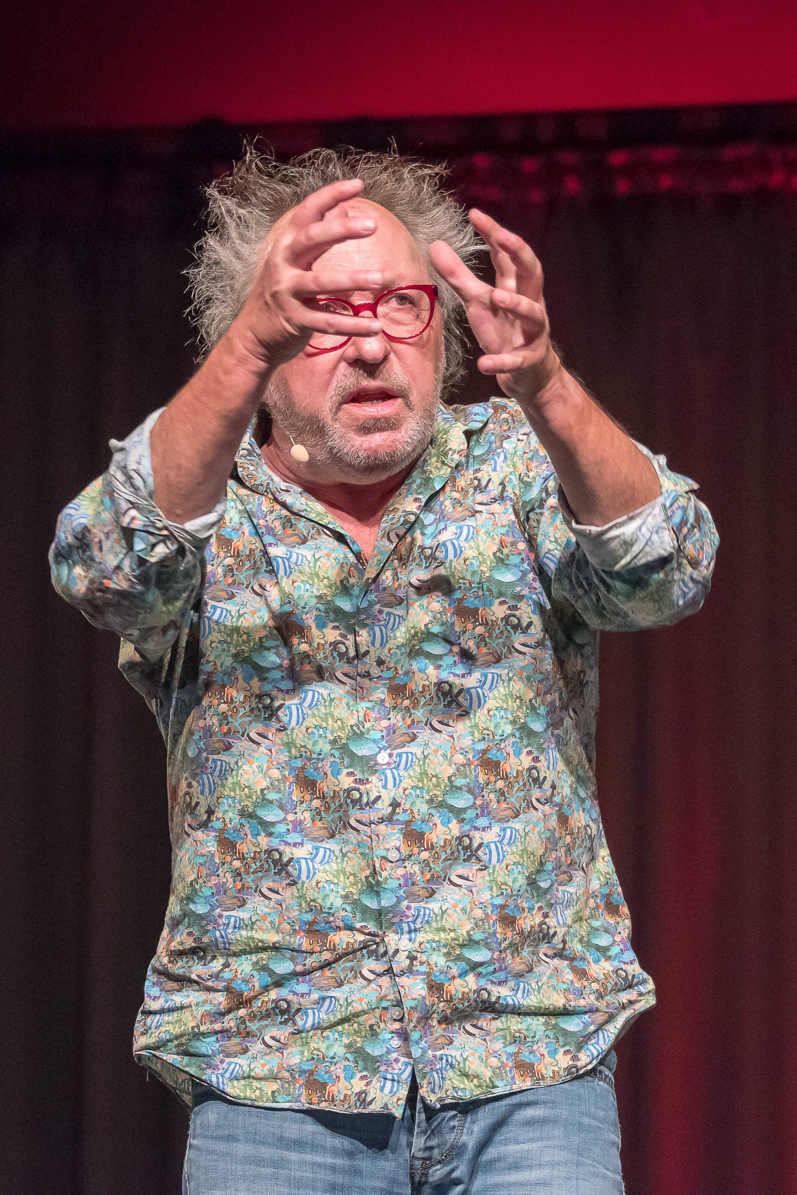 Urban Priol Ein Mann in buntem Hemd, zerzaustem Haar und Brille. Er hält die Hände, wie eine Kugel vor sein Gesicht.