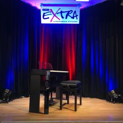 Zu sehen ist nur die Bühne vom Café Extra mit Beleuchtung. Das ePiano mit Hocker steht mittig auf der Bühne.