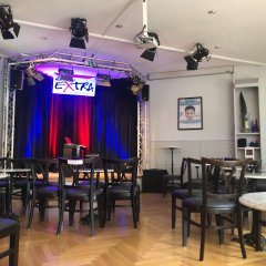 Zu sehen ist der bestuhlte Saal und die Bühne vom Café Extra mit Beleuchtung. Das ePiano mit Hocker steht mittig auf der Bühne.