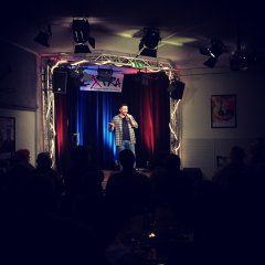 Ein jüngerer Mann mit Mikro in der Hand steht auf der Bühne.