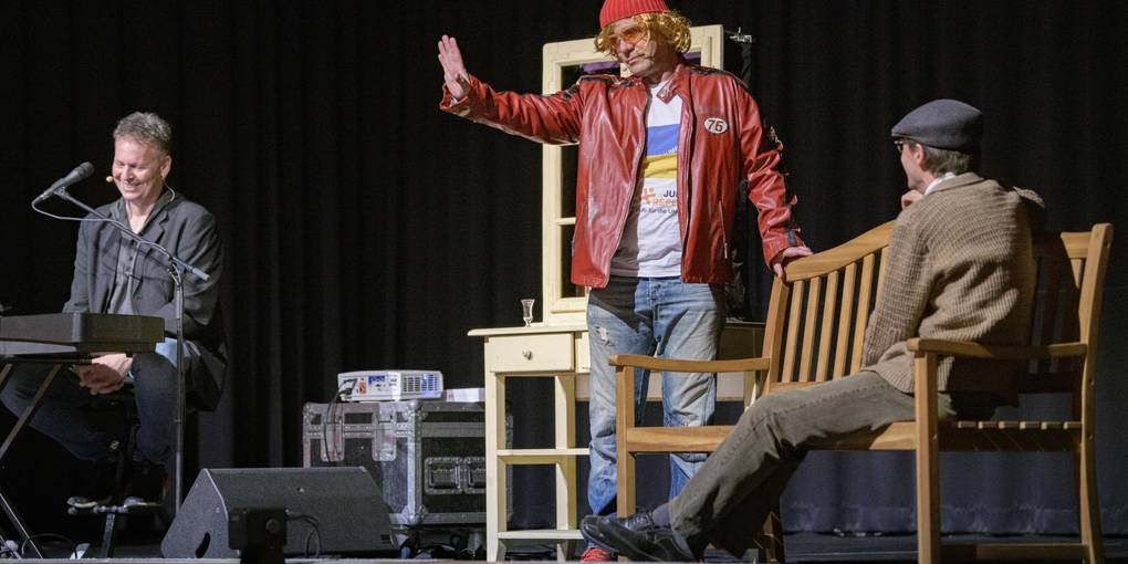 Drei Männer sind auf der Bühne im Volkshaus Büttelborn. Ralf Baiting sitzt ganz links im Bild am Klavier. Christian Döring sitzt auf der Babbelbank rechts und Udo Döring steht dazwischen. 