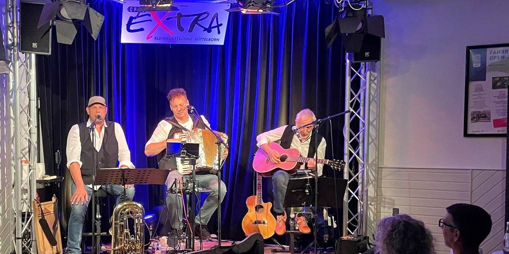 Fred Kraus, Ralf Baiting und Bodo Kolbe sitzen auf der Bühne und machen Musik.