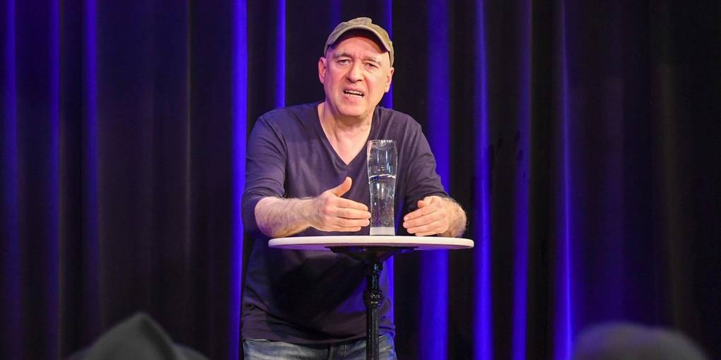 Butzko steht hinter einem Stehtisch auf der Café Extra Bühne. Er spricht zum Publikum.