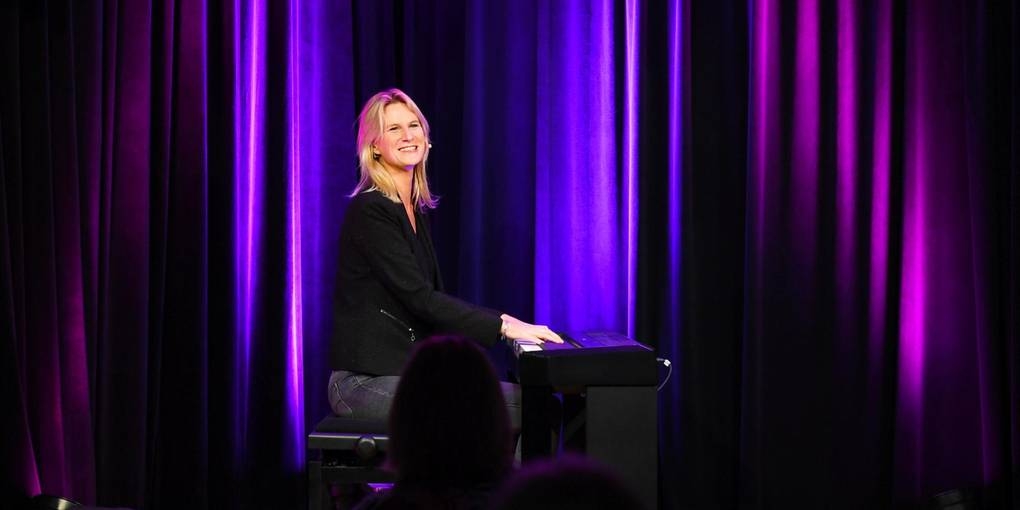 Lucy sitzt am Klavier auf der Café Extra Bühne und singt, dabei schaut sie ins Publikum.